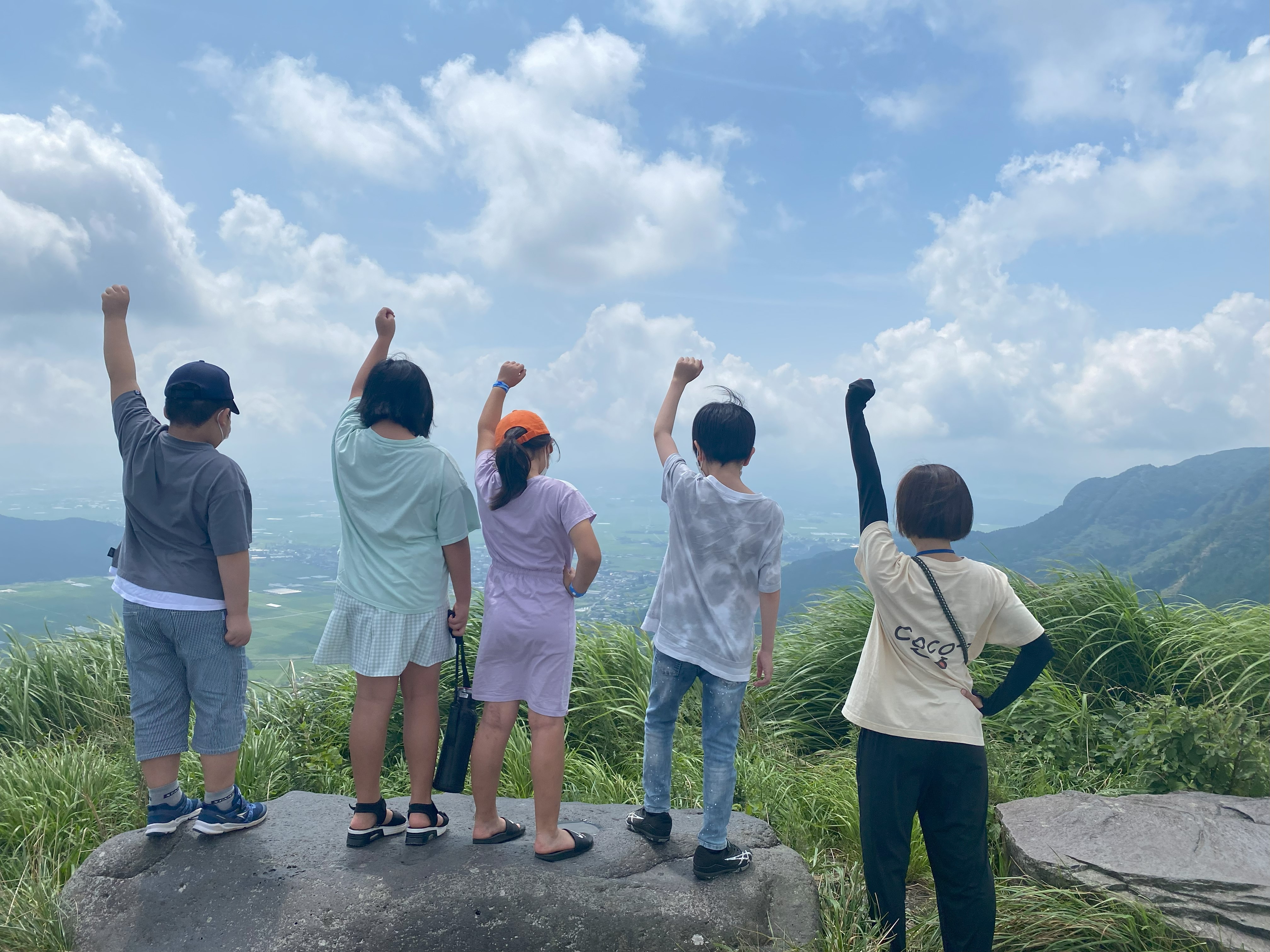 こどもたちが見晴らしの良い場所で拳を突き上げている背後からの写真